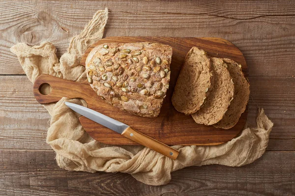 Вид зверху свіжий домашній нарізаний хліб з насінням на дерев'яній дошці біля тканини і ножа — стокове фото