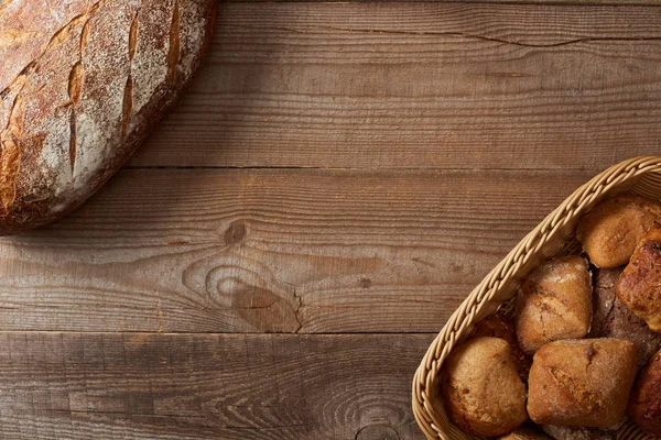 Верхний вид хлеба буханка и булочки в плетеной корзине на деревянный стол — стоковое фото