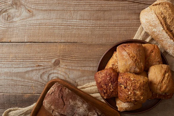 Vue de dessus des pains et petits pains sur tissu rustique sur table en bois — Photo de stock