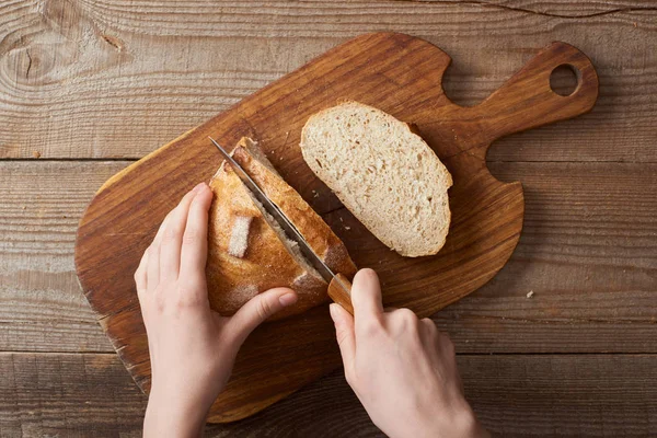 Partial view of woman slicing loaf of bread on wooden chopping board — Stock Photo
