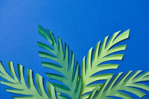 Вид зверху на зелений папір вирізає листя на синьому фоні з пробілом для копіювання — стокове фото