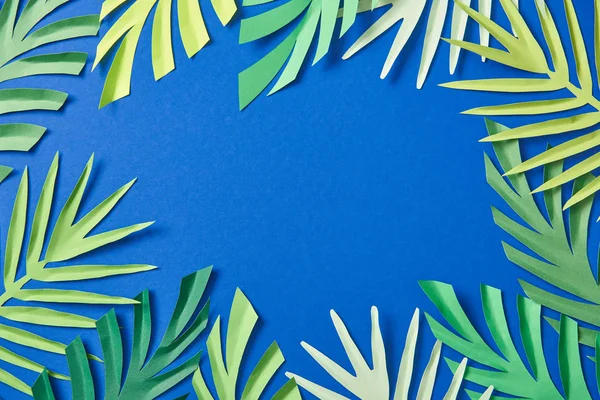 Vista superior do papel verde cortar folhas tropicais no fundo azul com espaço de cópia — Fotografia de Stock