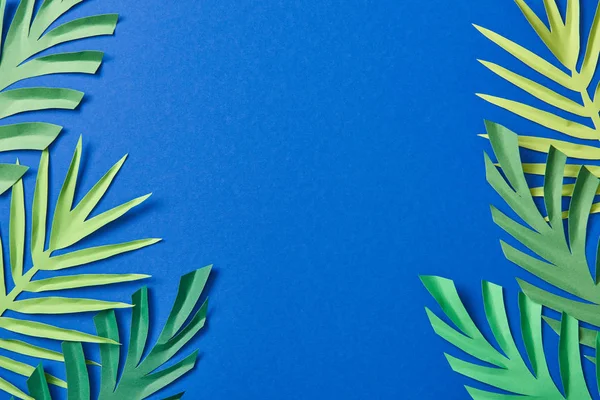 Top view of green paper cut exotic leaves on blue background with copy space — Stock Photo