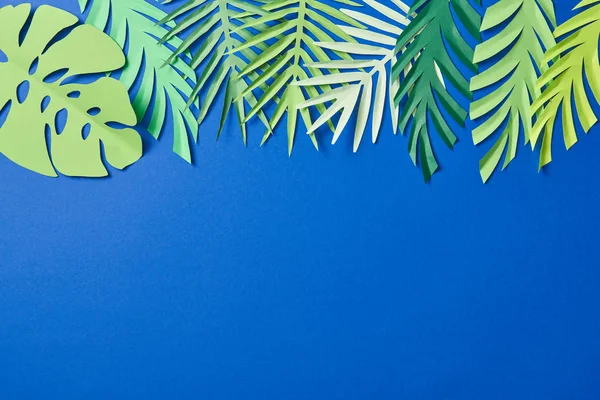 Vista superior de papel verde cortar hojas exóticas sobre fondo azul con espacio de copia - foto de stock