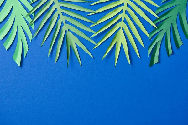 Vista superior de papel verde cortar hojas exóticas sobre fondo azul con espacio de copia - foto de stock