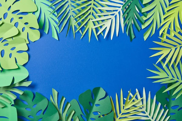 Vue du dessus du papier vert feuilles exotiques sur fond bleu avec espace de copie — Photo de stock
