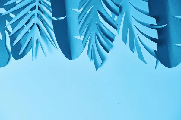 Top view of blue minimalistic paper cut palm leaves on blue background with copy space — Stock Photo