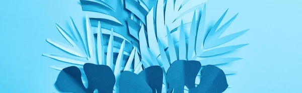 Panoramic shot of blue minimalistic paper cut palm leaves on blue background — Stock Photo