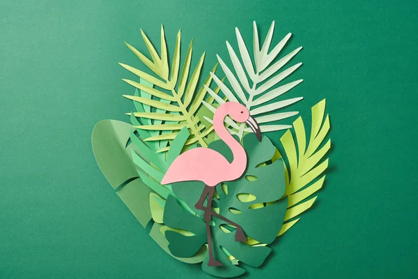 Top view of paper cut palm leaves and pink flamingo on green background — Stock Photo