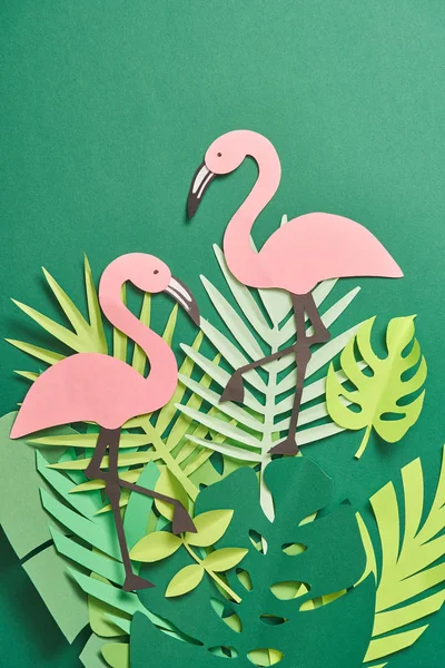 Top view of exotic paper cut palm leaves and pink flamingos on green background with copy space — Stock Photo