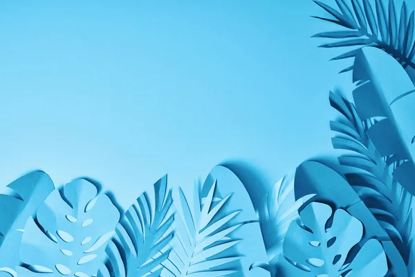 Top view of blue exotic paper cut palm leaves on blue background with copy space — Stock Photo