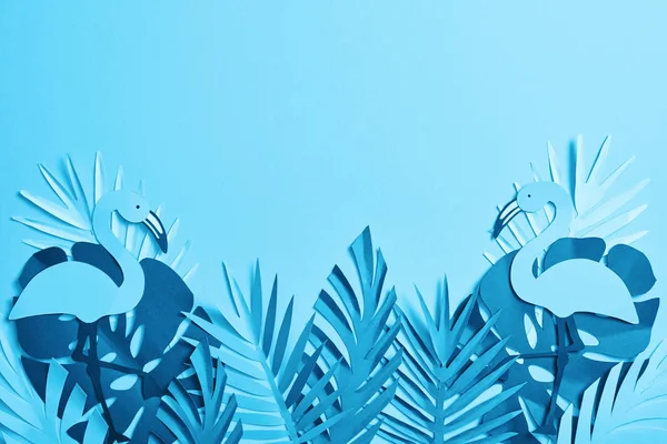 Top view of blue paper cut palm leaves and flamingos on blue background with copy space — Stock Photo