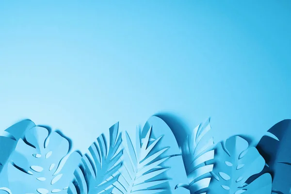 Vue du dessus des feuilles de palmier découpées en papier exotique bleu sur fond bleu avec espace de copie — Photo de stock