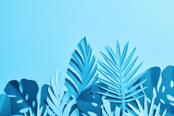 Top view of blue exotic paper cut palm leaves on blue background with copy space — Stock Photo