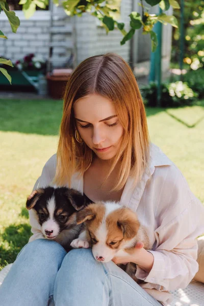 Blonde girl in garden with adorable puppies at sunny day — Stock Photo