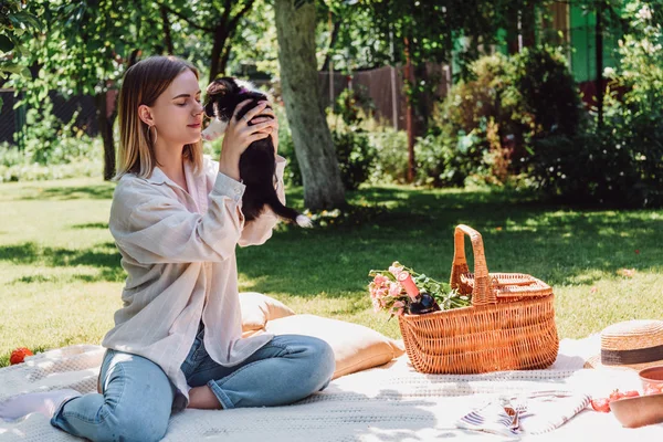 Блондинка сидить на ковдрі в саду і тримає цуценя в сонячний день — стокове фото