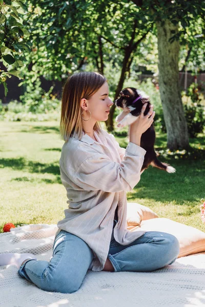 Blonde girl with closed eyes holding cute puppy while sitting in green garden — Stock Photo