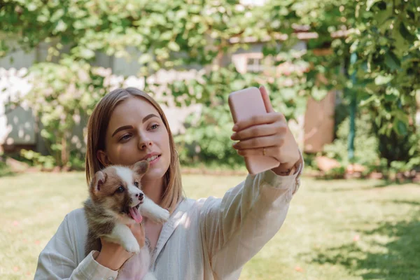 Menina loira no jardim verde levando selfie com cachorrinho bonito — Fotografia de Stock