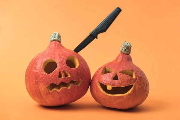 Spooky Halloween pumpkins with knife on orange background — Stock Photo