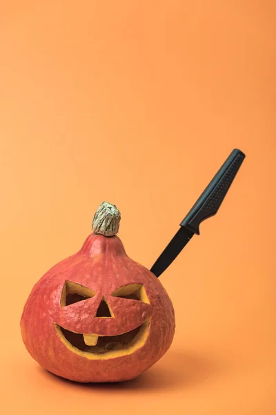 Spooky Halloween pumpkin with knife on orange background — Stock Photo