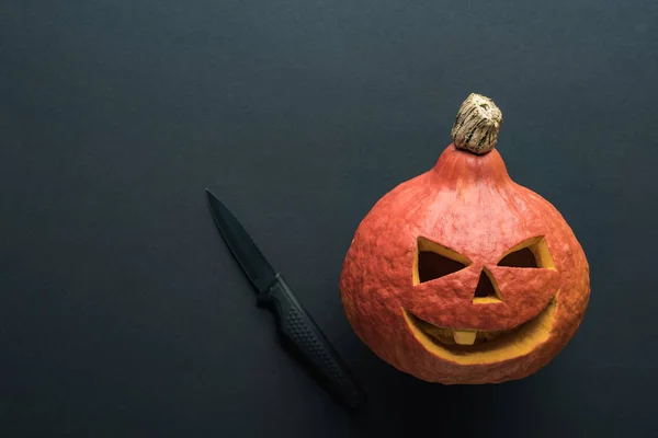 Top view of carved spooky Halloween pumpkin with knife on black background — Stock Photo