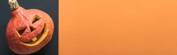 Vista dall'alto della zucca di Halloween spettrale intagliata su sfondo nero e arancione, scatto panoramico — Stock Photo