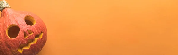 Сверху вид на жуткий резной Хэллоуин тыква на оранжевом фоне, панорамный снимок — стоковое фото