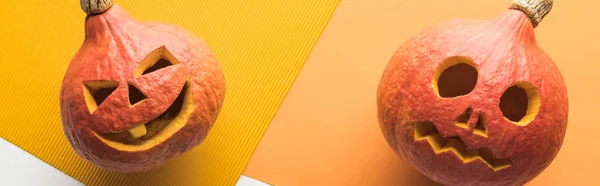 Top view of carved spooky pumpkins on white and orange background, panoramic shot — Stock Photo