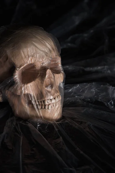Espeluznante cráneo humano en celofán sobre fondo negro, decoración de Halloween - foto de stock
