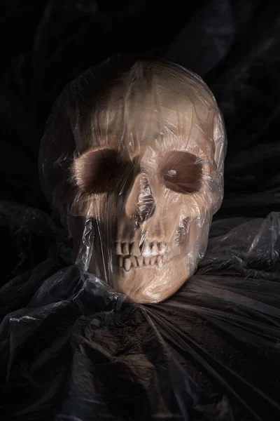 Spooky human skull in cellophane on black background, Halloween decoration — Stock Photo