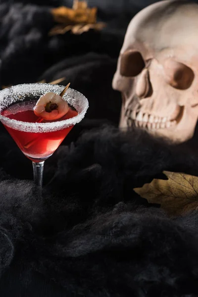 Cocktail rouge près du crâne et des feuilles jaunes sèches d'érable sur fond noir — Photo de stock