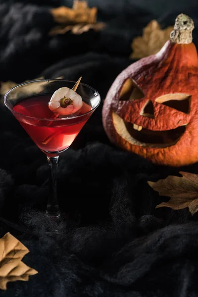 Red cocktail near Halloween pumpkin and maple dry yellow leaves on black background — Stock Photo