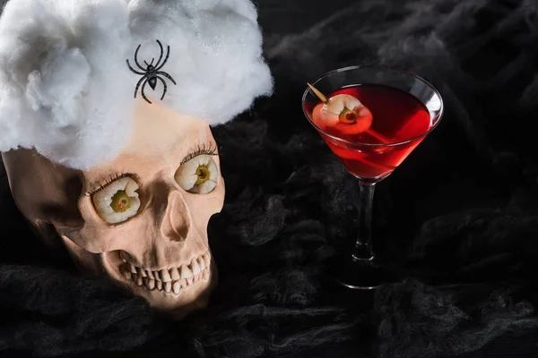 Красный коктейль возле жуткого черепа с пауком на черном фоне — стоковое фото