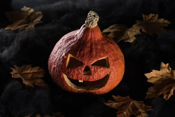 Spooky carved Halloween pumpkin on black background with foliage — Stock Photo
