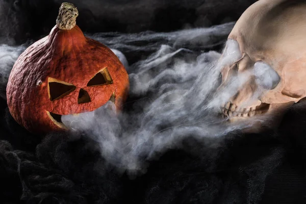 Spooky human skull and carved Halloween pumpkin on black background — Stock Photo