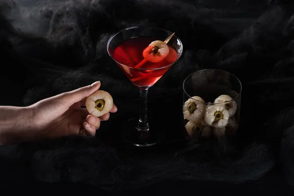 Abgeschnittene Ansicht einer Frau mit Dekoration in der Nähe eines roten Halloween-Cocktails in schwarzen Wolken — Stockfoto