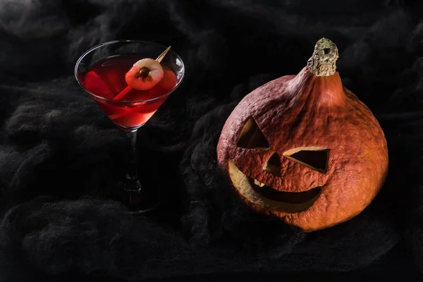 Red decorated Halloween cocktail near spooky pumpkin in black clouds — Stock Photo