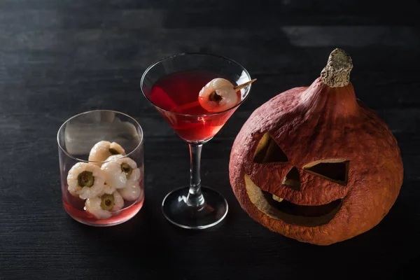 Spooky carved Halloween pumpkin and red cocktail on black background — Stock Photo