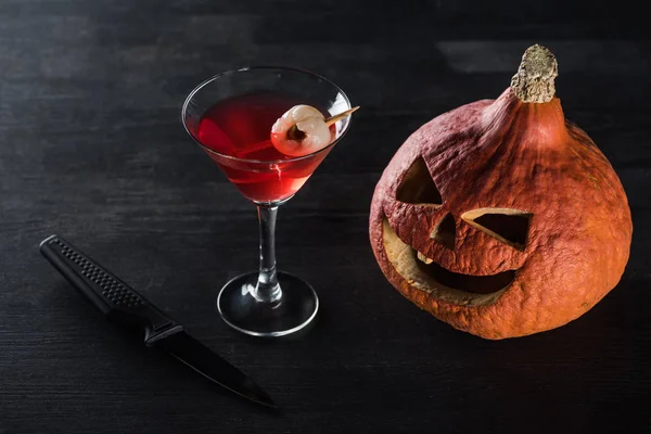 Assustador Halloween abóbora, faca e coquetel vermelho no fundo preto — Fotografia de Stock