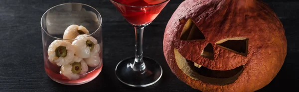 Panoramic shot of spooky Halloween pumpkin and red cocktail on black background — Stock Photo