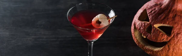 Panoramic shot of carved Halloween pumpkin and red cocktail on black background — Stock Photo