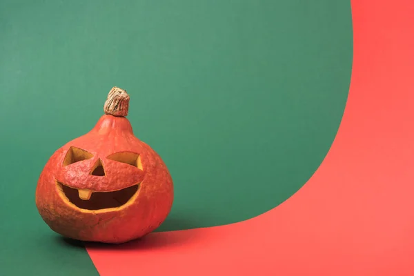 Spooky Halloween pumpkin on red and green background — Stock Photo