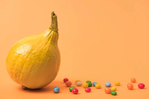 Zucca dipinta di colore giallo con caramelle su sfondo arancione — Foto stock