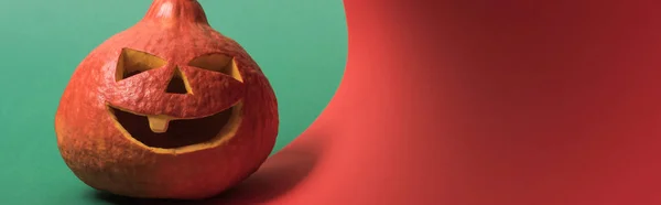 Plano panorámico de espeluznante calabaza de Halloween sobre fondo rojo y verde - foto de stock