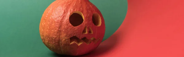 Plano panorámico de espeluznante calabaza de Halloween sobre fondo rojo y verde - foto de stock