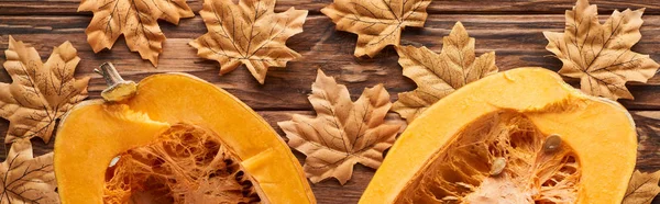 Panoramic shot of pumpkin halves on brown wooden surface with dried autumn leaves — Stock Photo