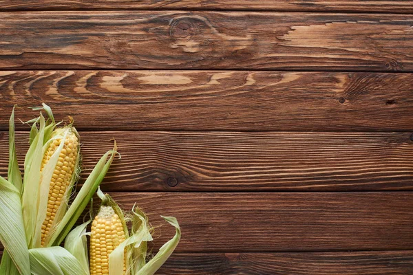 Top view of raw corn on brown wooden surface with copy space — Stock Photo