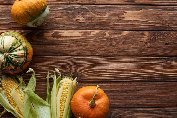 Top view of fresh ripe pumpkin and sweet corn on brown wooden surface with copy space — Stock Photo