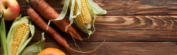 Panoramic shot of fresh ripe apples, carrots and sweet corn on brown wooden surface with copy space — Stock Photo