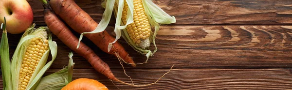 Plan panoramique de pommes fraîches mûres, de carottes et de maïs sucré sur une surface en bois brun avec espace de copie — Photo de stock